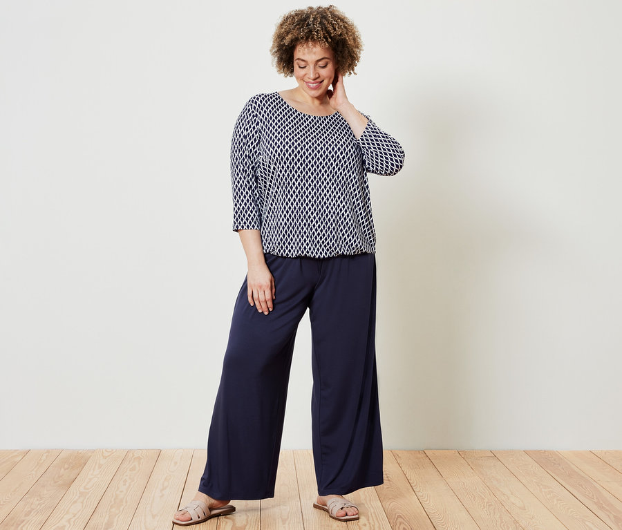 Femme posant en blouse imprimée et pantalon palazzo bleu foncé.