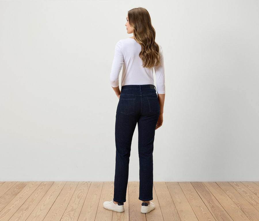 Une femme, vue de dos, porte un jean foncé, un t-shirt blanc à manches trois-quarts et des baskets blanches.