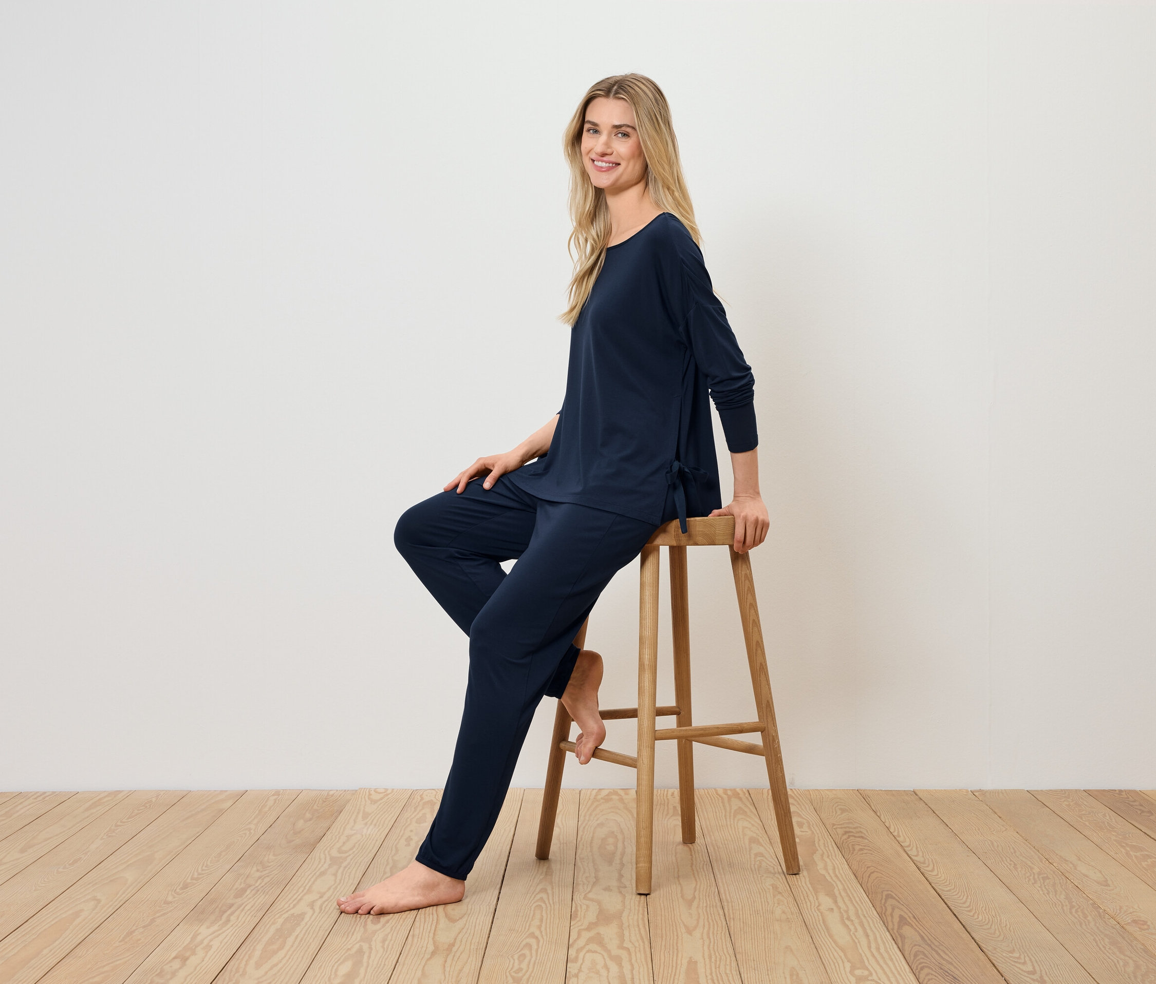 Une femme blonde est assise sur un tabouret en bois et porte un pyjama bleu marine.