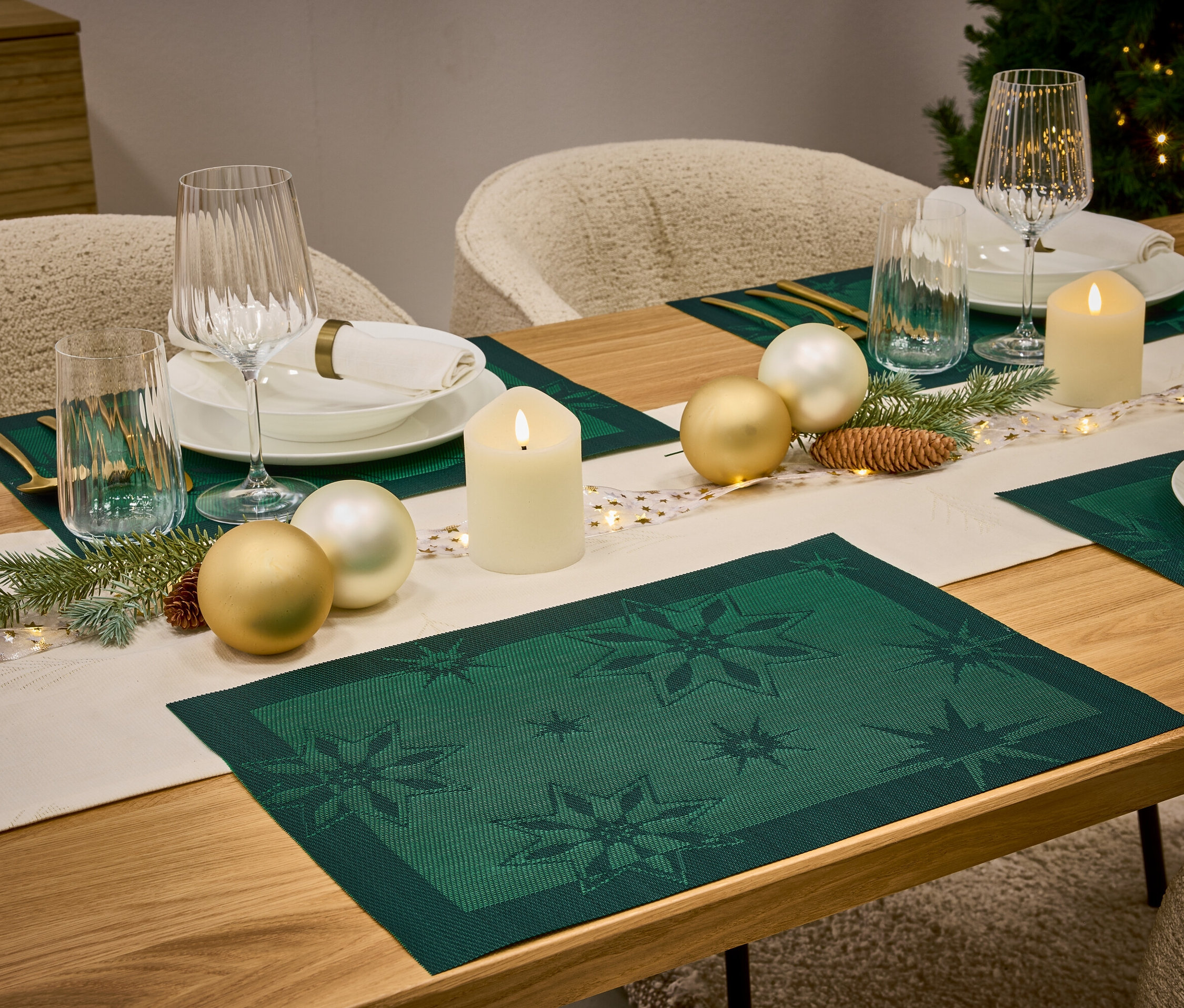 Table dressée avec des sets de table vert foncé à motifs d'étoiles, des assiettes blanches, des verres, des bougies et des décorations.