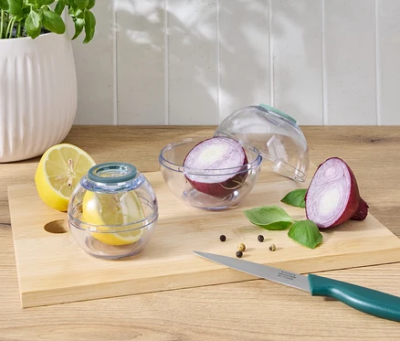 Moitié de citron dans un récipient transparent à côté d'une moitié de citron et d'un demi oignon rouge dans un récipient transparent à côté d'un demi oignon rouge sur une planche à découper avec un couteau.