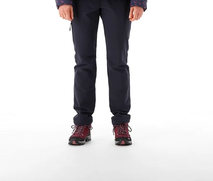 Femme debout, portant un bonnet noir, une doudoune matelassée bleu foncé à motifs avec une doublure rouge, un Pantalon CMP pour femmes en polyester stretch bleu foncé et des chaussures de randonnée bordeaux.