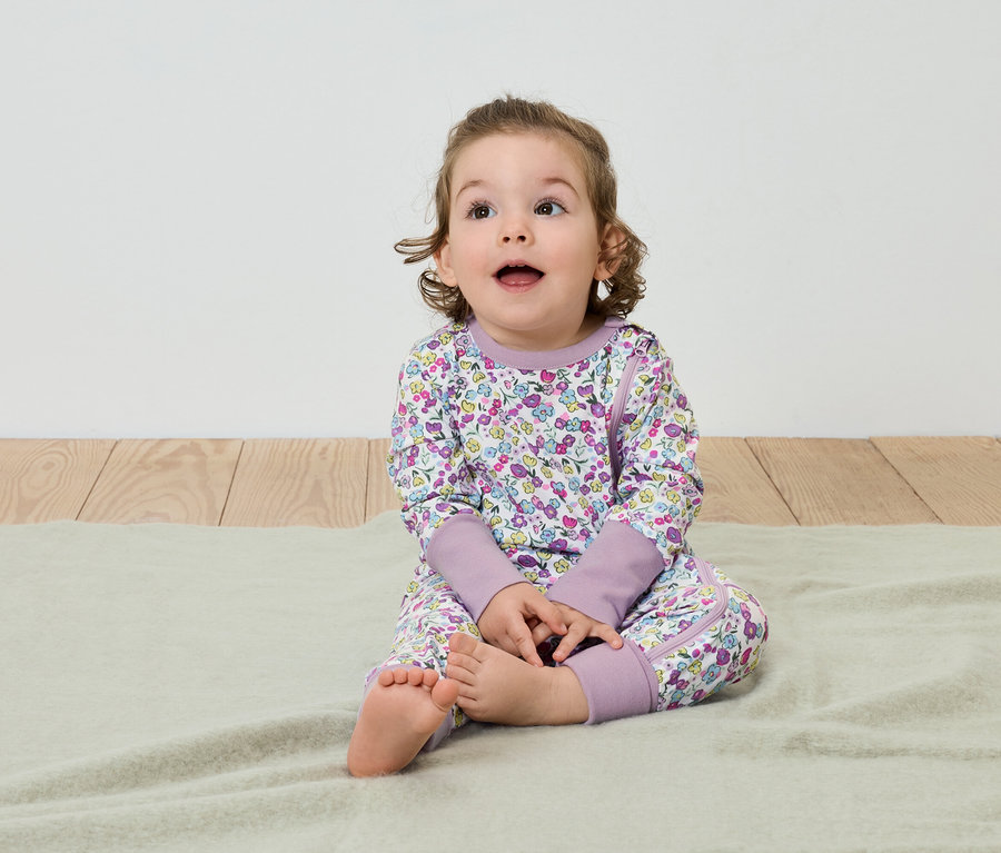 Un enfant est assis sur une couverture et porte un pyjama à fleurs.