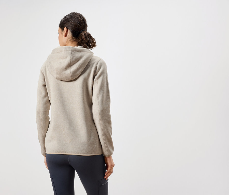 Vue de dos, une femme porte un sweat à capuche beige et un pantalon bleu foncé.