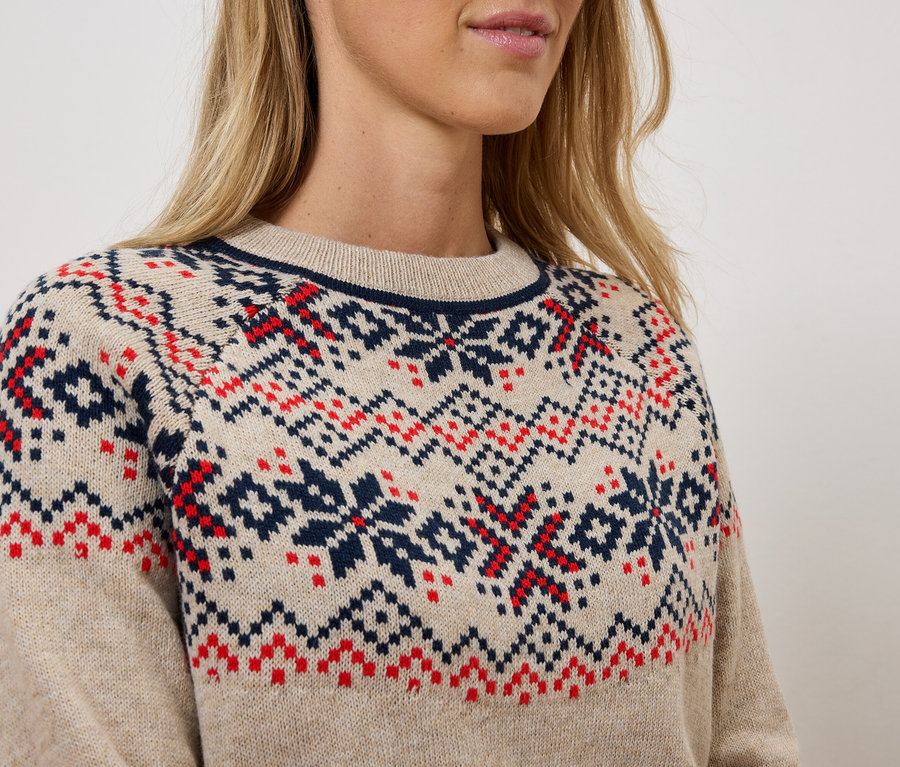 Gros plan d'une femme portant un pull en tricot beige avec des motifs géométriques rouges et bleus.