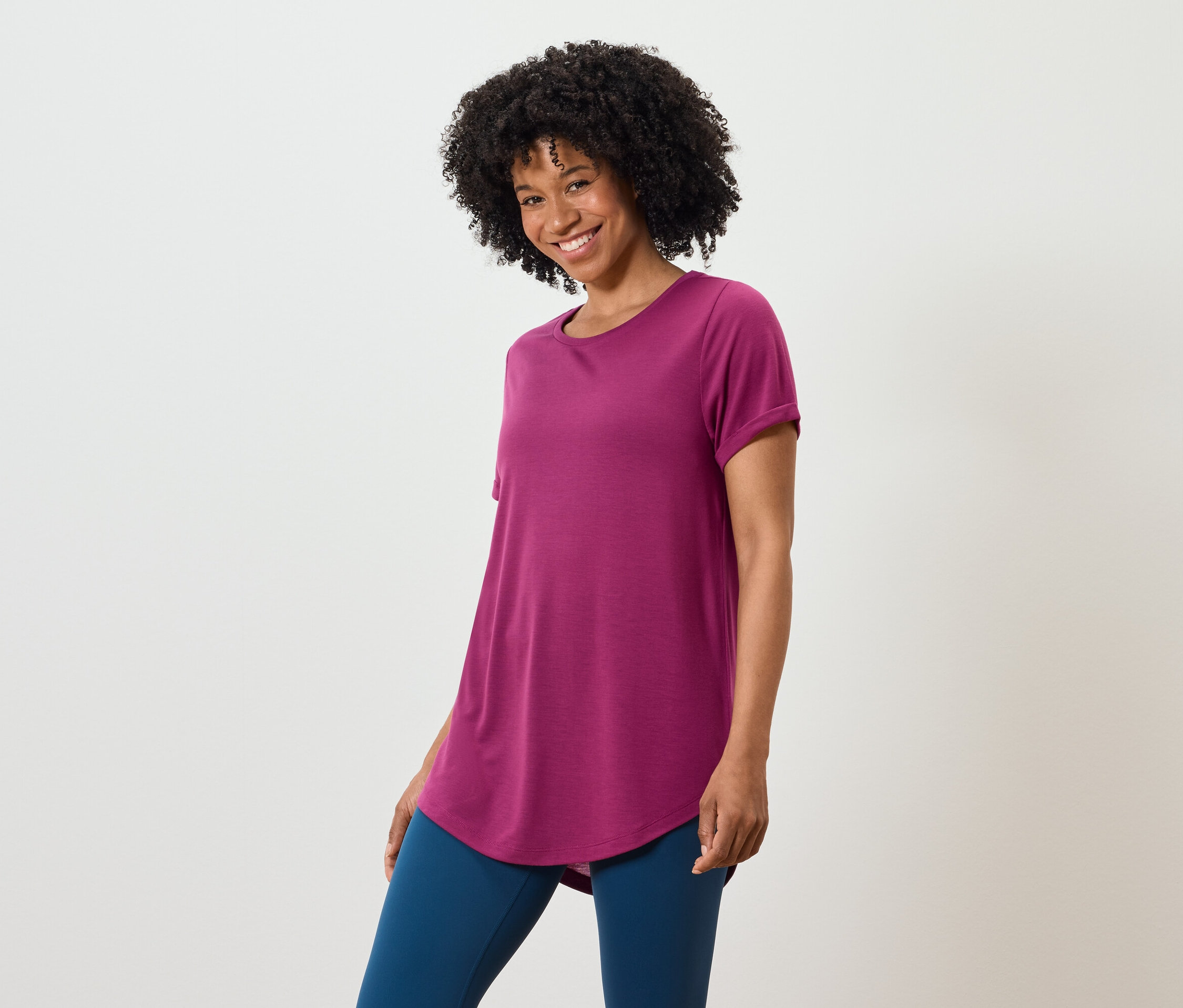 Une femme aux cheveux bouclés foncés porte un t-shirt violet et un legging bleu.