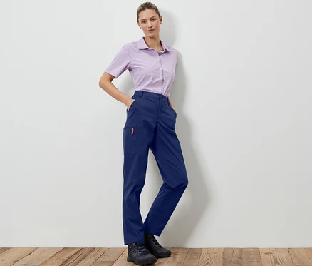 Une femme pose en pantalon outdoor pliable bleu foncé et une chemise lilas clair.