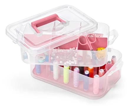 Une boîte à outils à plusieurs niveaux en plastique transparent avec des accents roses, remplie d'accessoires de couture.