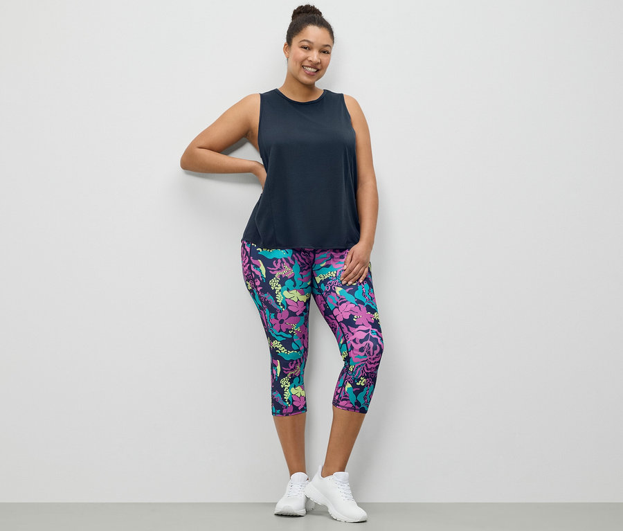 Une femme pose, portant un débardeur de sport bleu foncé et un collant de sport 3/4 avec un imprimé.