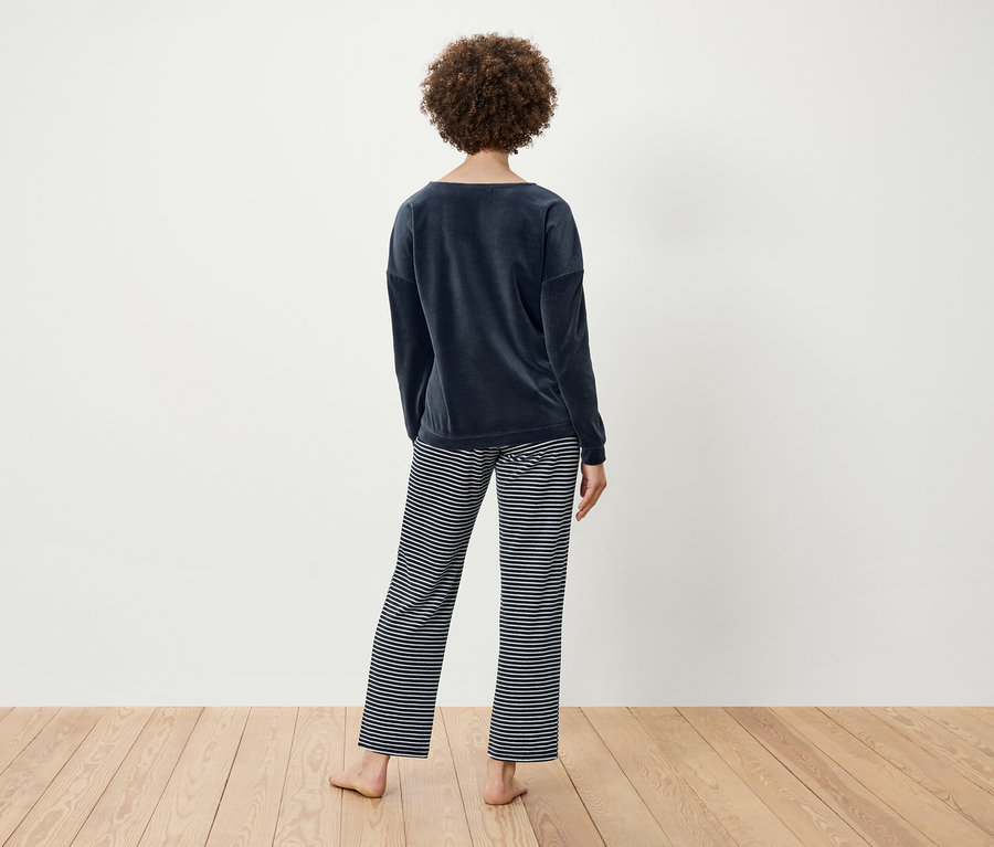 Une femme aux cheveux bouclés, vue de dos, porte un haut en velours bleu marine et un pantalon rayé.