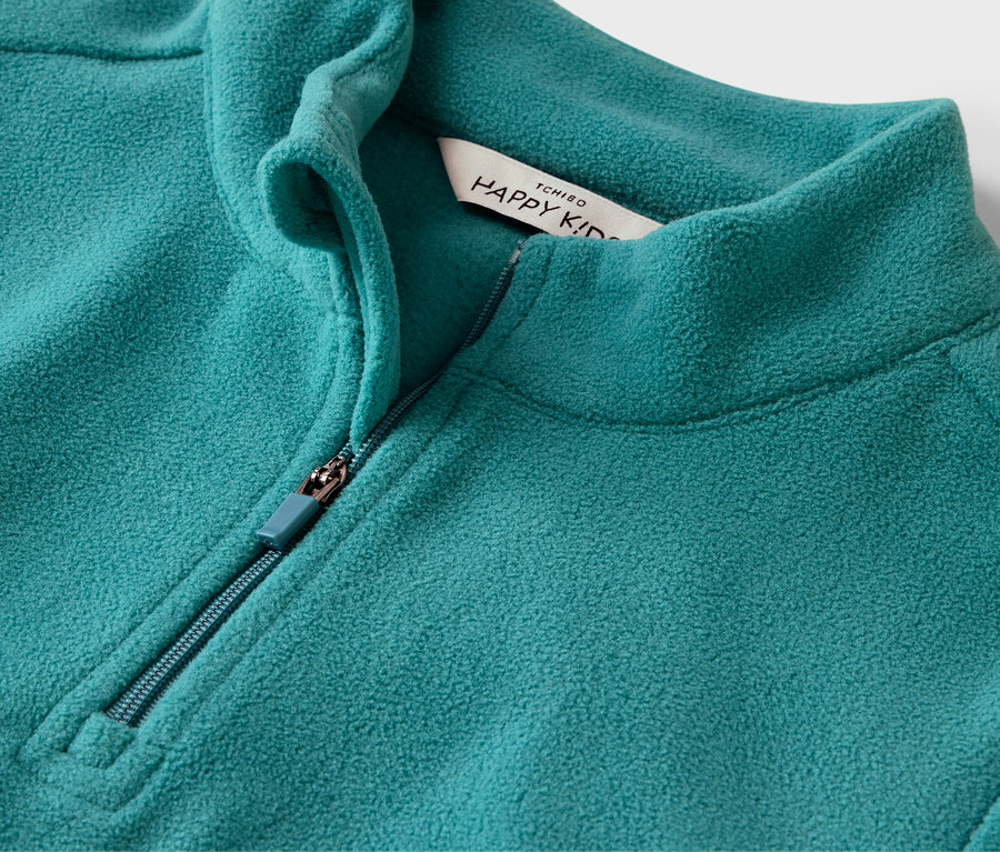 Gros plan d'un pull en polaire turquoise avec fermeture éclair et étiquette Happy Kid.
