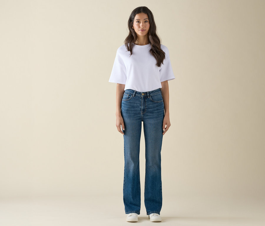 Une femme debout portant un t-shirt blanc, un jean bleu et des baskets blanches.
