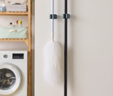 Un plumeau et un balai sont accrochés au mur, avec une machine à laver et une étagère en arrière-plan.