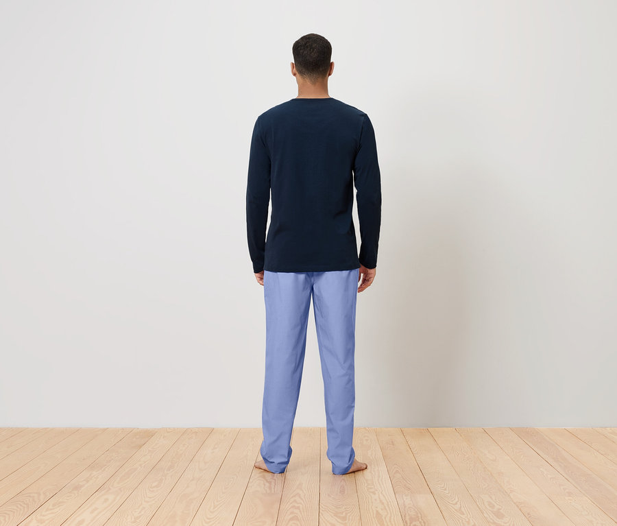 Un homme se tient dos à la caméra, portant un T-shirt à manches longues bleu foncé et un pantalon bleu clair.