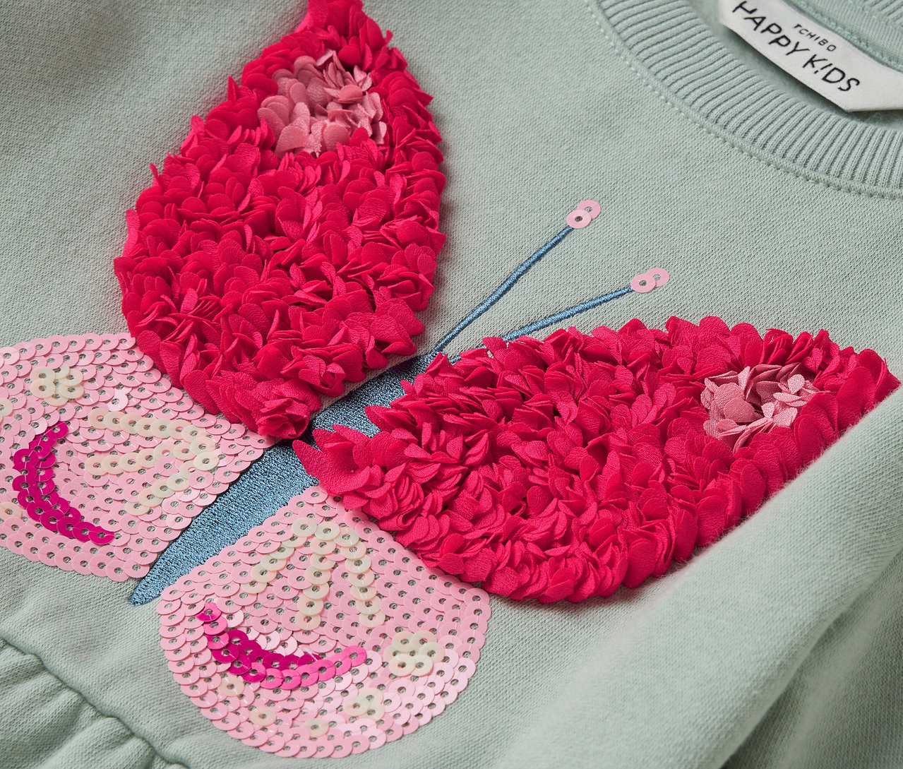 Robe vert clair avec application papillon avec paillettes roses et fleurs rouges.