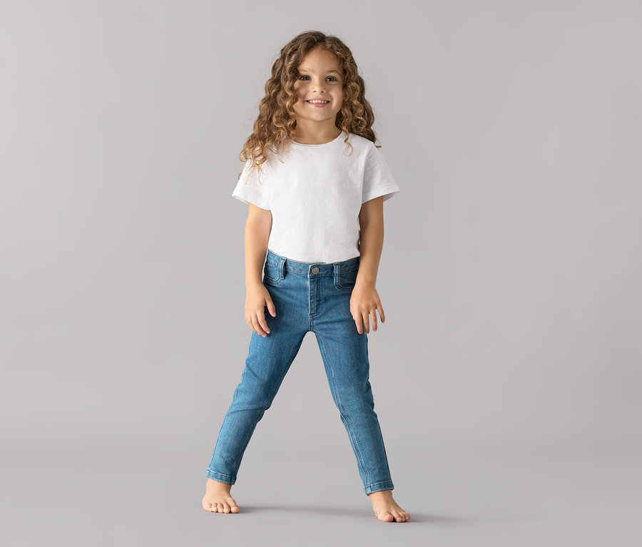 Fillette portant un t-shirt blanc et un jean pour enfant ‒ Fit «
Lotta
» debout sur un fond gris.