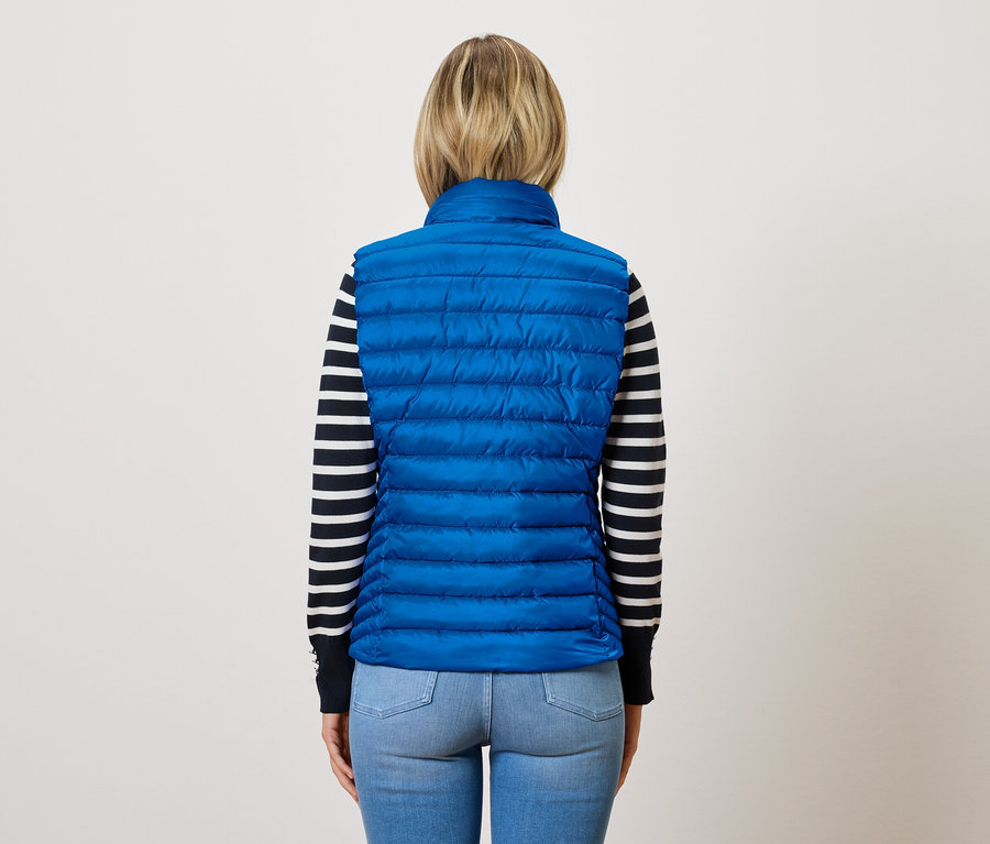 Une femme, vue de dos, porte un gilet matelassé bleu sur un pull rayé.