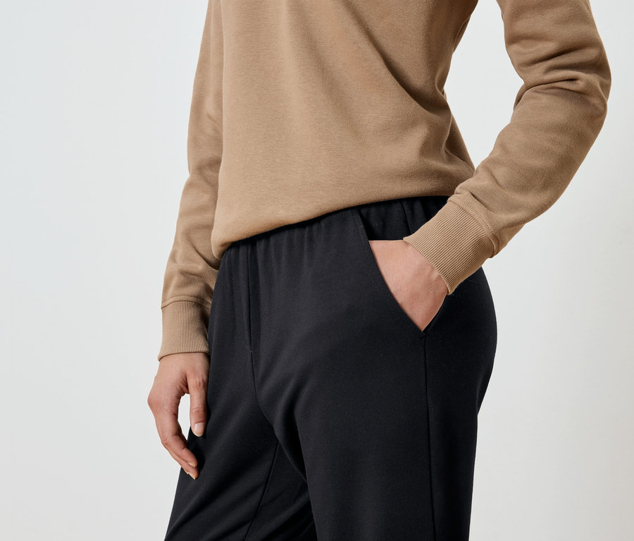 Gros plan d'une femme avec sa main dans la poche d'un pantalon de jogging noir et d'un sweat-shirt beige.
