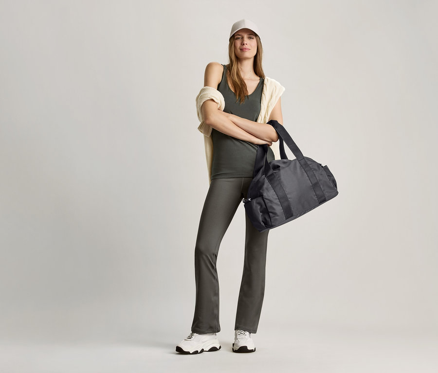 Femme posant dans un haut vert olive et un sac de sport noir.