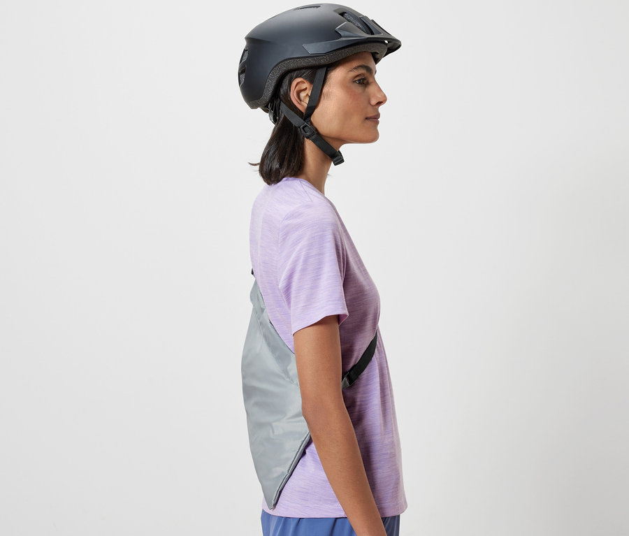 Vue latérale d'une femme portant un casque de vélo avec des sacs à provisions pour vélo sur l'épaule.