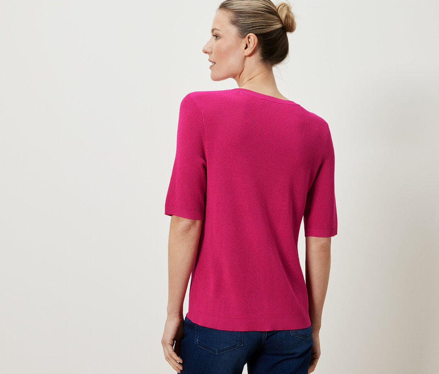Une femme porte un cardigan rose en maille fine avec du lin.