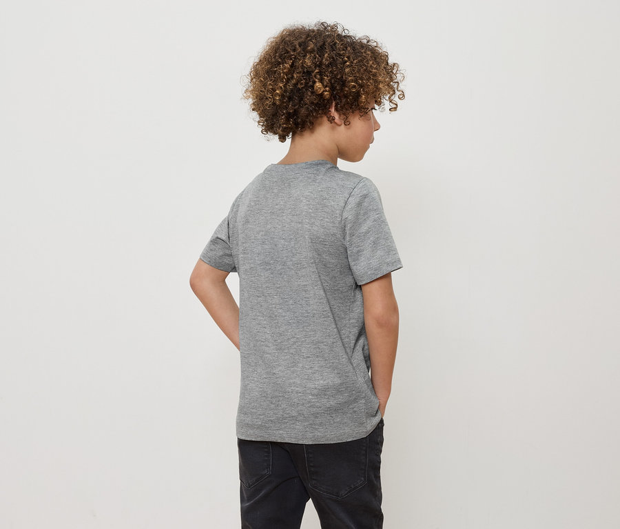 Un garçon aux cheveux bouclés, vu de dos, porte un t-shirt gris et un jean noir.