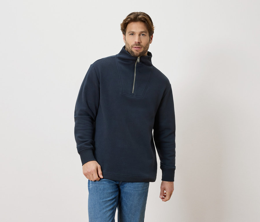 Un homme porte un pull bleu marine zippé et un jean bleu.