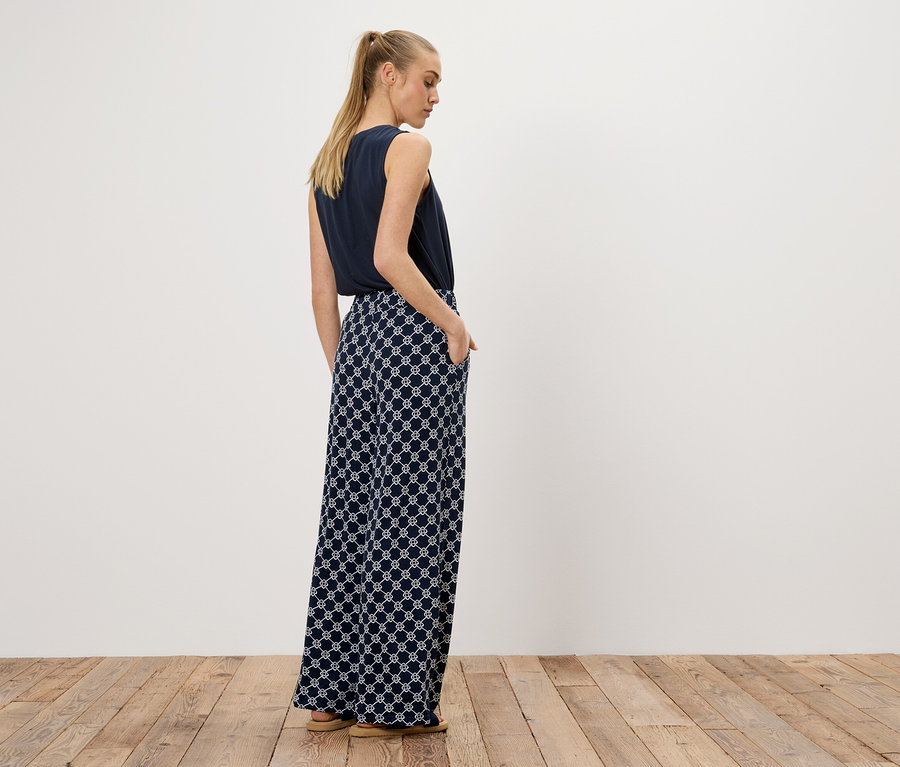 Une femme se tient dos à la caméra, portant un haut bleu marine et un pantalon large avec un motif géométrique blanc.
