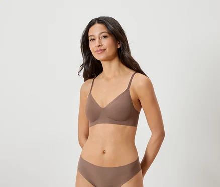 Femme brune portant un soutien-gorge et une culotte marron, posant les mains derrière le dos.
