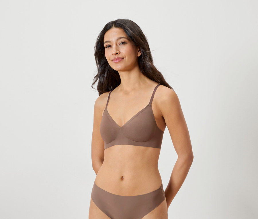 Femme brune portant un soutien-gorge et une culotte marron, posant les mains derrière le dos.