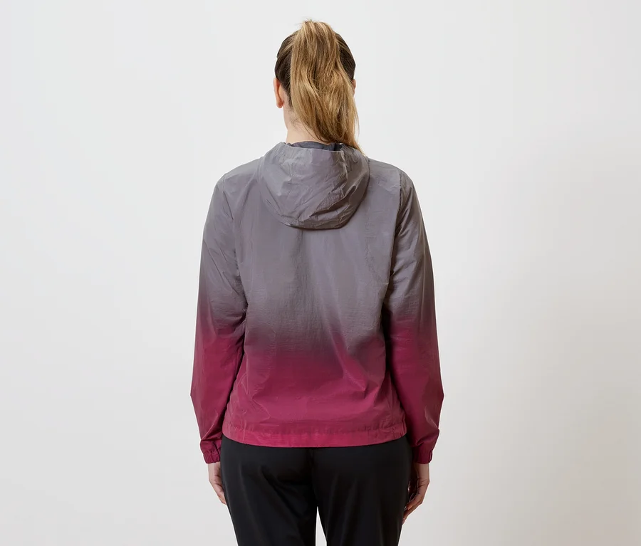 Vue arrière d'une femme avec une queue de cheval portant une veste à capuche avec un dégradé de gris à rose et un pantalon noir.