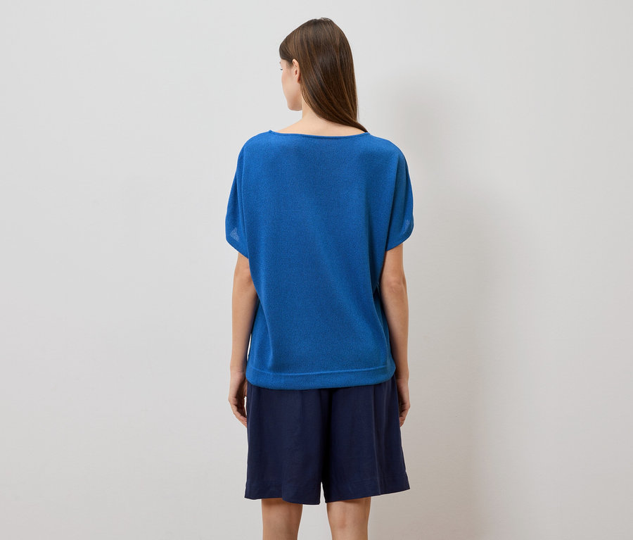 Vue arrière d'une femme aux longs cheveux bruns portant un t-shirt bleu et un short bleu marine sur un fond blanc.