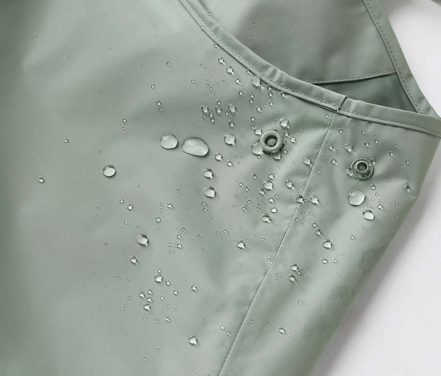 Gros plan sur un tissu vert clair imperméable avec des gouttes d'eau et deux boutons-pression.