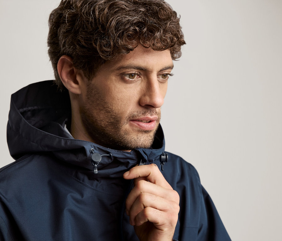 Homme aux cheveux bouclés portant une veste à capuche bleu marine.