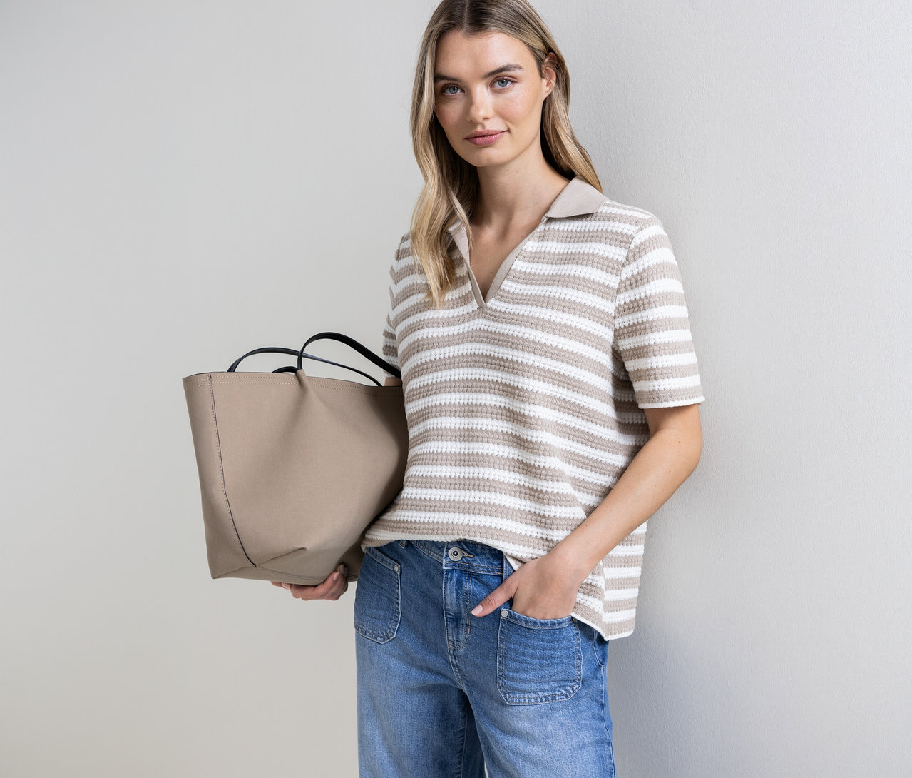 Femme tenant un sac beige et portant un pull en maille rayé Street One. Une main dans la poche.