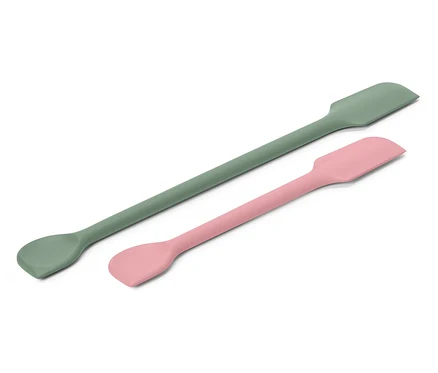 Une spatule verte et une spatule rose sont disposées en diagonale sur un fond blanc.