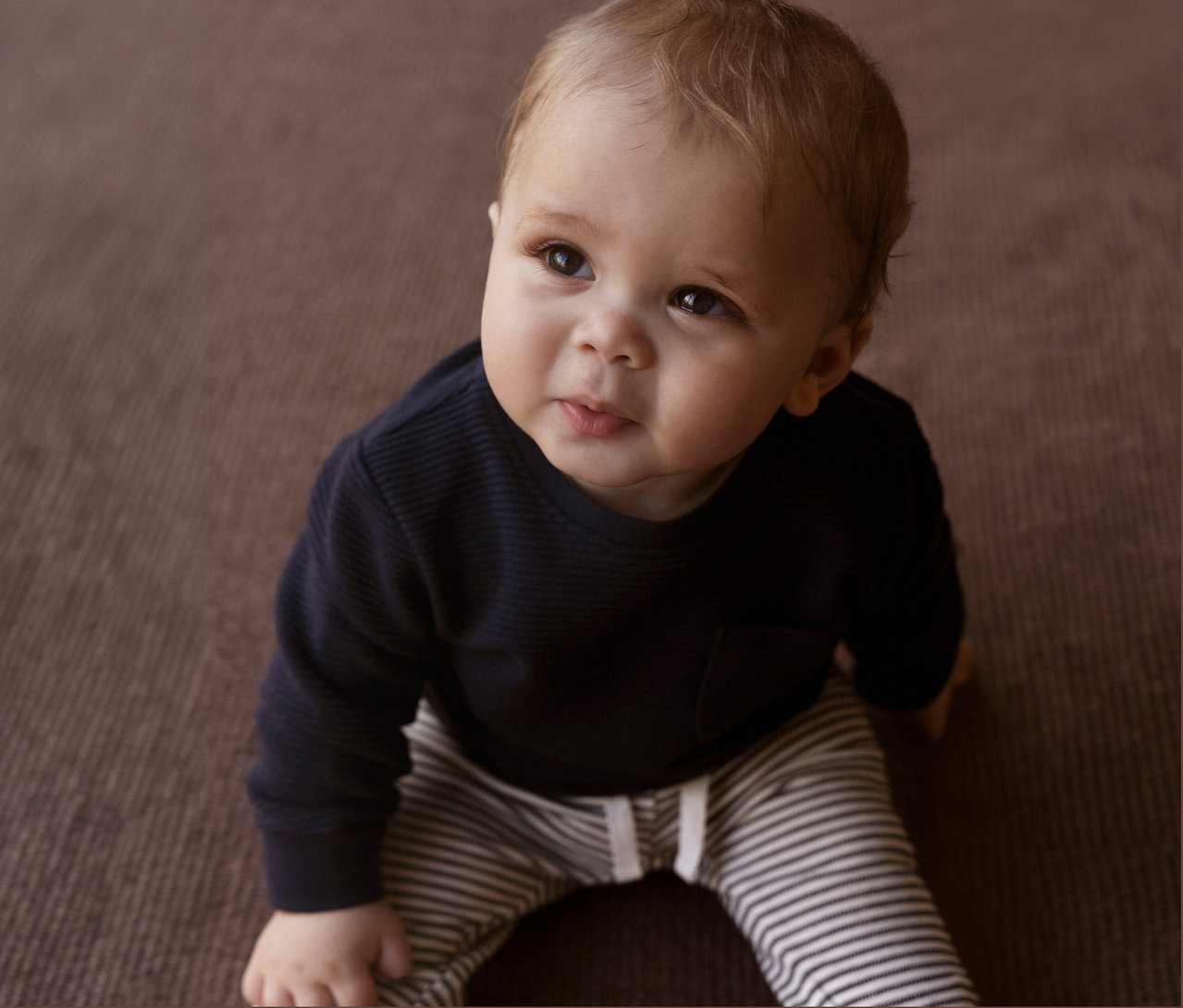 Bébé assis sur le sol portant un pantalon en jersey bébé NAME IT rayé.