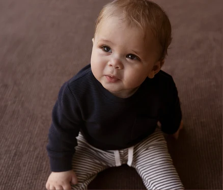 Bébé assis sur le sol portant un pantalon en jersey bébé NAME IT rayé.