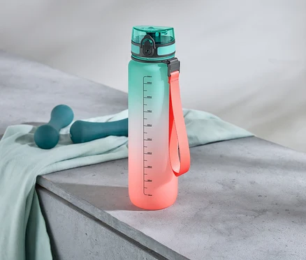 Une bouteille d'eau avec un dégradé de couleurs se tient à côté de deux haltères sur un tissu.