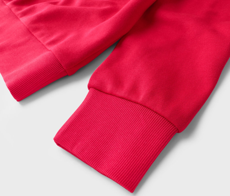 Gros plan des manches d'un pull rouge avec des poignets côtelés sur un fond blanc.