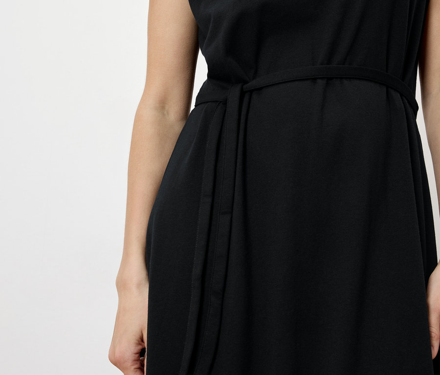 Gros plan d'une femme portant une robe noire avec une ceinture sur fond blanc.