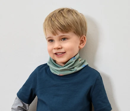 Un garçon souriant aux cheveux blonds et portant un t-shirt bleu porte un foulard vert à motifs animaliers.