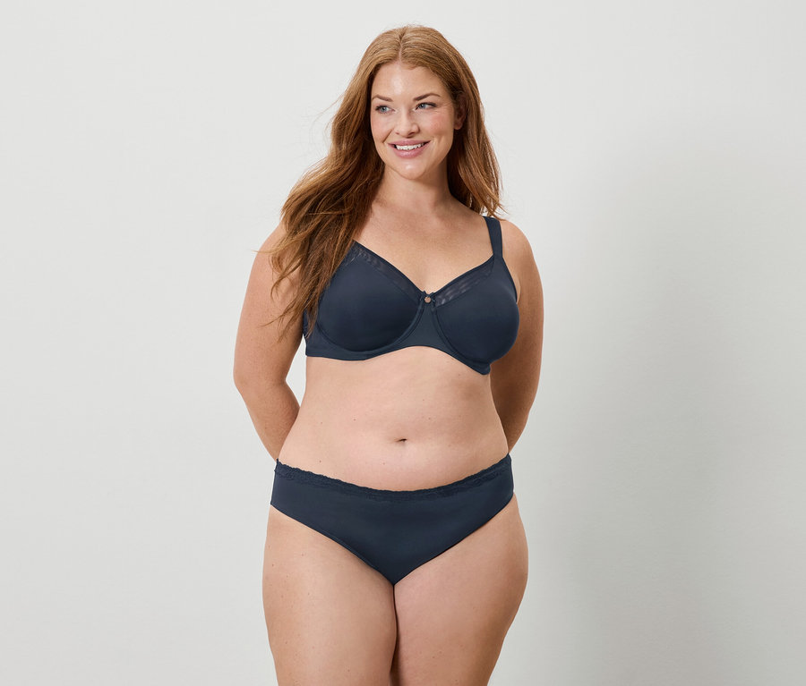 Femme aux longs cheveux roux portant un soutien-gorge et une culotte bleu marine, souriant.