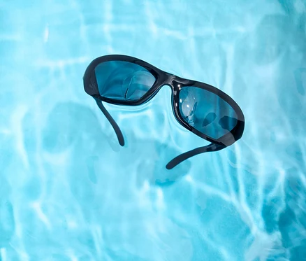 Des lunettes de soleil noires flottent dans l'eau bleu clair.
