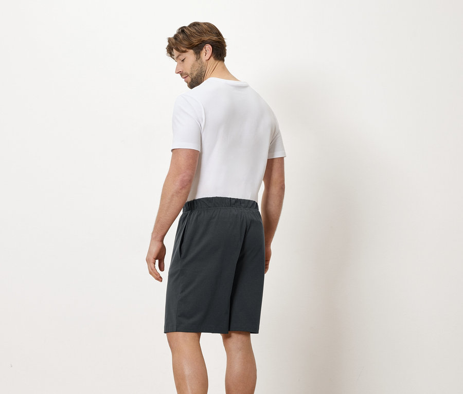 Homme de dos portant un t-shirt blanc et un short gris sur fond blanc.