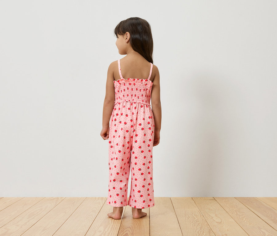 Une jeune fille, vue de dos, porte une combinaison rose à motifs de fraises.
