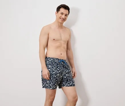 Un homme en maillot de bain debout devant un mur blanc.
