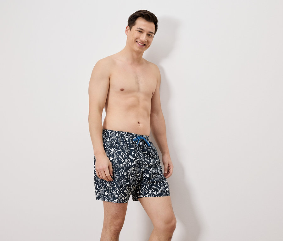 Un homme en maillot de bain debout devant un mur blanc.