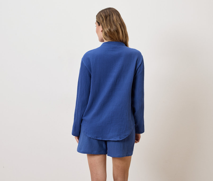 Vue arrière d'une femme aux longs cheveux bruns portant une chemise bleue à manches longues et un short.