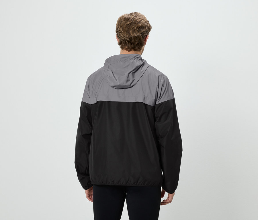 Vue arrière d'un homme aux cheveux bouclés portant un imperméable gris et noir et un pantalon noir sur fond blanc.